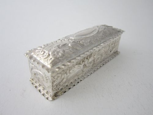 fig 1. A small rectangular Victorian sterling silver trinket box featuring embossed floral scrolls, scalloped edges, and a blank central cartouche on the hinged lid.