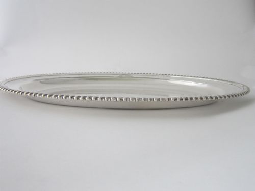 fig 2. An oval William IV sterling silver meat platter featuring a decorative gadrooned border and an engraved coat of arms on the upper rim.