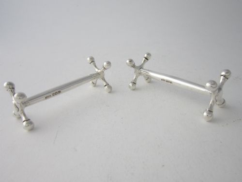 fig 1. A pair of hallmarked sterling silver knife rests with crossed spherical end supports connected by a smooth central bar.