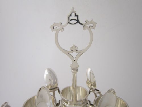 fig 1. An antique George V sterling silver egg cruet featuring a central carrying handle, six egg cups, and matching spoons arranged on an oval tray base.