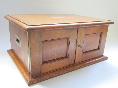 fig 1. An open oak cutlery canteen with double doors revealing three fitted drawers filled with sterling silver flatware and featuring brass campaign handles.