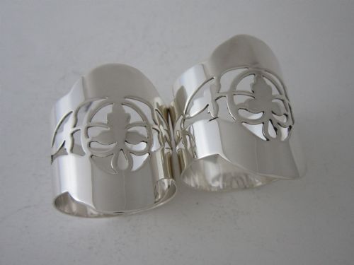 fig 1. A pair of polished sterling silver napkin rings featuring pierced fretwork crest designs and shaped borders.