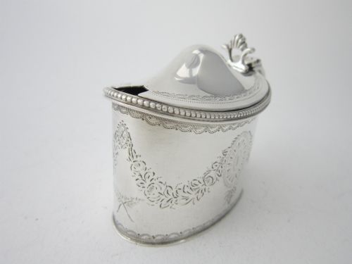 fig 2. An antique George V sterling silver mustard pot featuring intricate garland engraving, a hinged lid, C-scroll handle, and an included silver spoon.