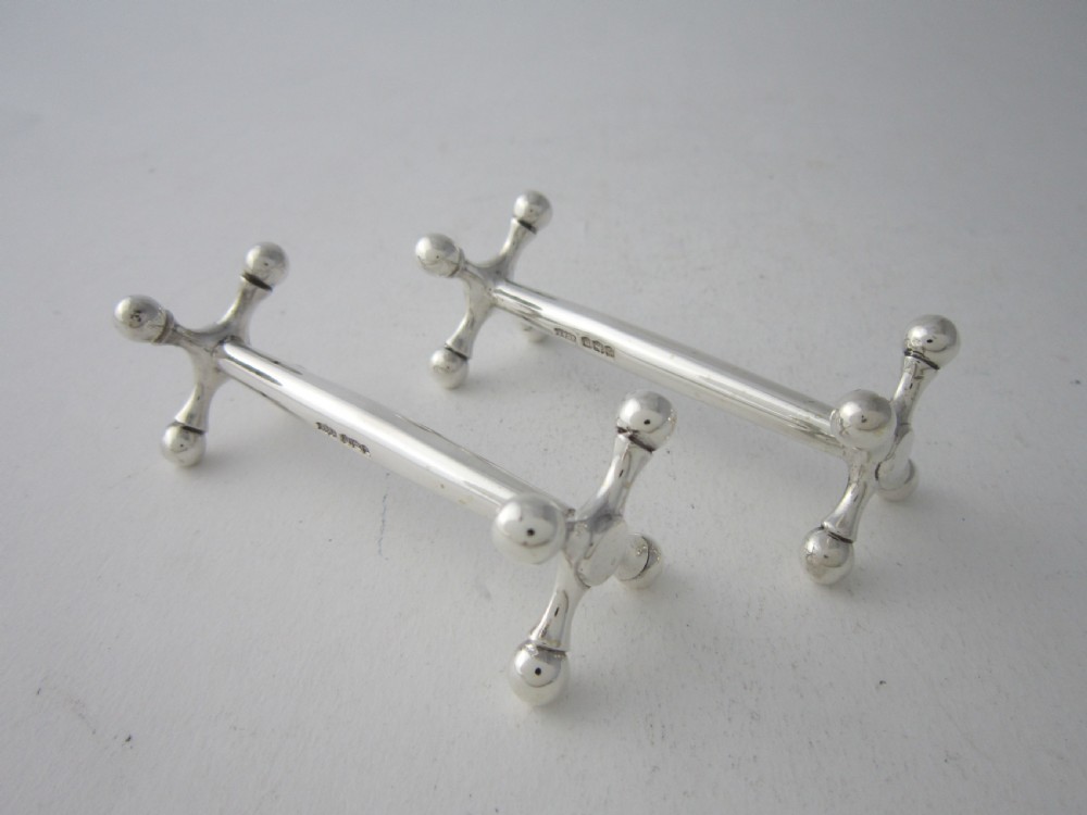 A pair of solid sterling silver knife rests featuring crossed X-shaped end supports with spherical terminals joined by a horizontal central bar.