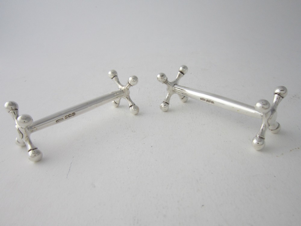 A pair of solid sterling silver knife rests featuring crossed X-shaped end supports with spherical terminals joined by a horizontal central bar. View II