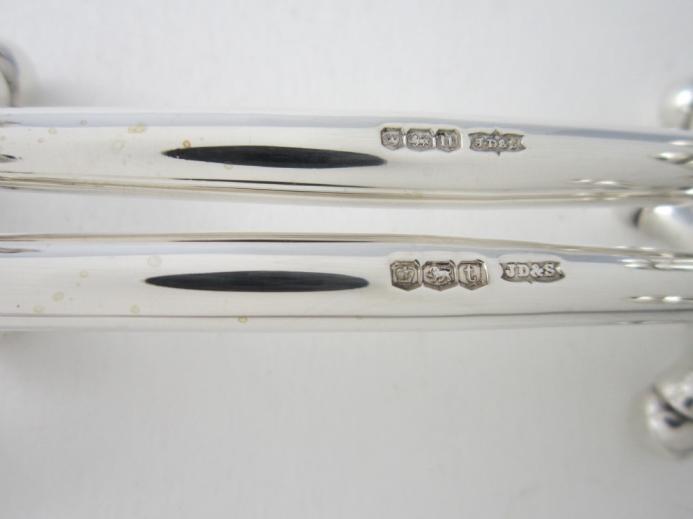 A pair of solid sterling silver knife rests featuring crossed X-shaped end supports with spherical terminals joined by a horizontal central bar. View IV