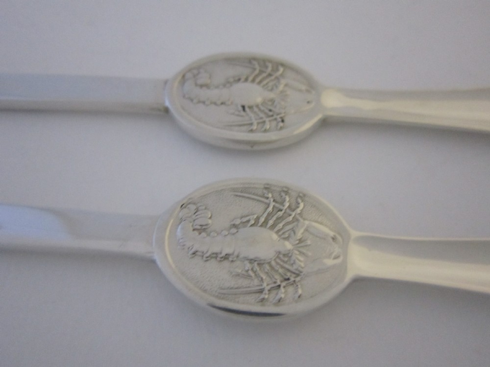 A pair of sterling silver lobster picks with embossed central medallions displayed inside an open black velvet-lined box. View VII