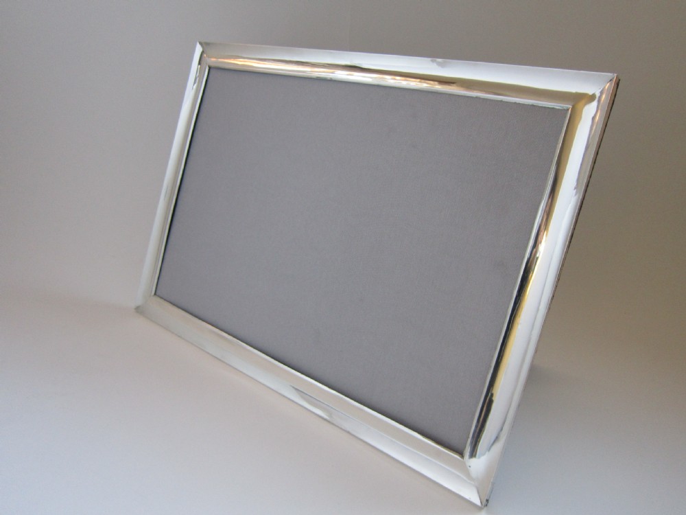 A large rectangular sterling silver picture frame with a simple moulded border and a grey fabric insert in a landscape alignment.