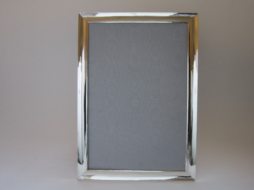 A large rectangular sterling silver picture frame with a simple moulded border and a grey fabric insert in a landscape alignment. View II