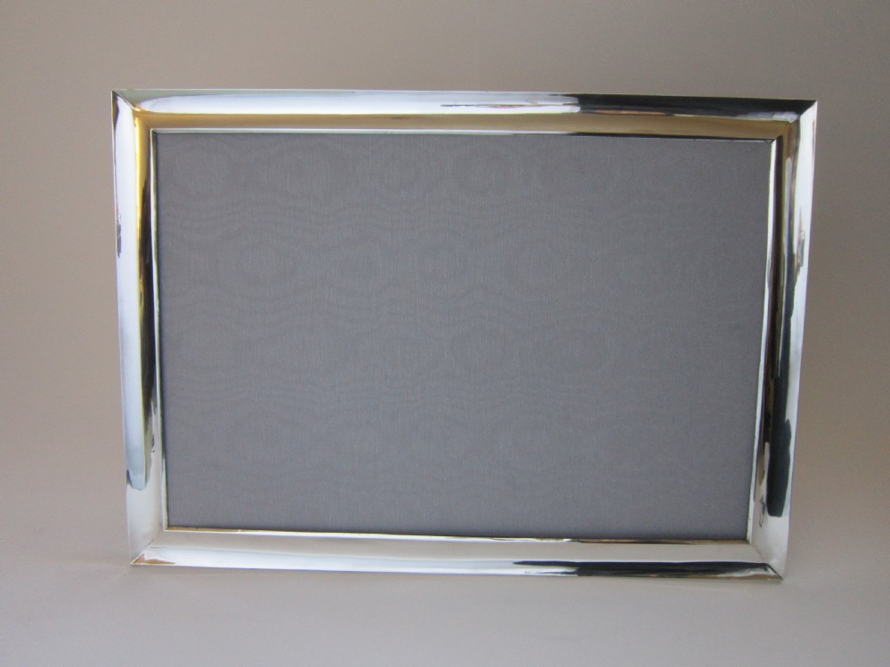 A large rectangular sterling silver picture frame with a simple moulded border and a grey fabric insert in a landscape alignment. View III