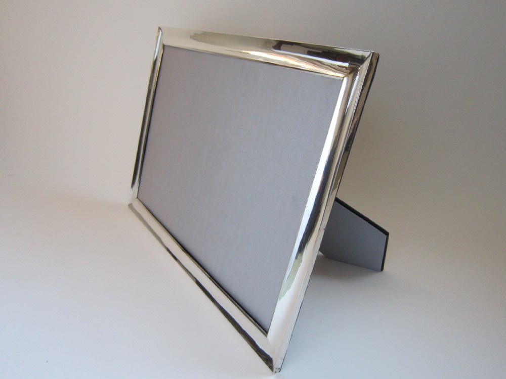 A large rectangular sterling silver picture frame with a simple moulded border and a grey fabric insert in a landscape alignment. View V