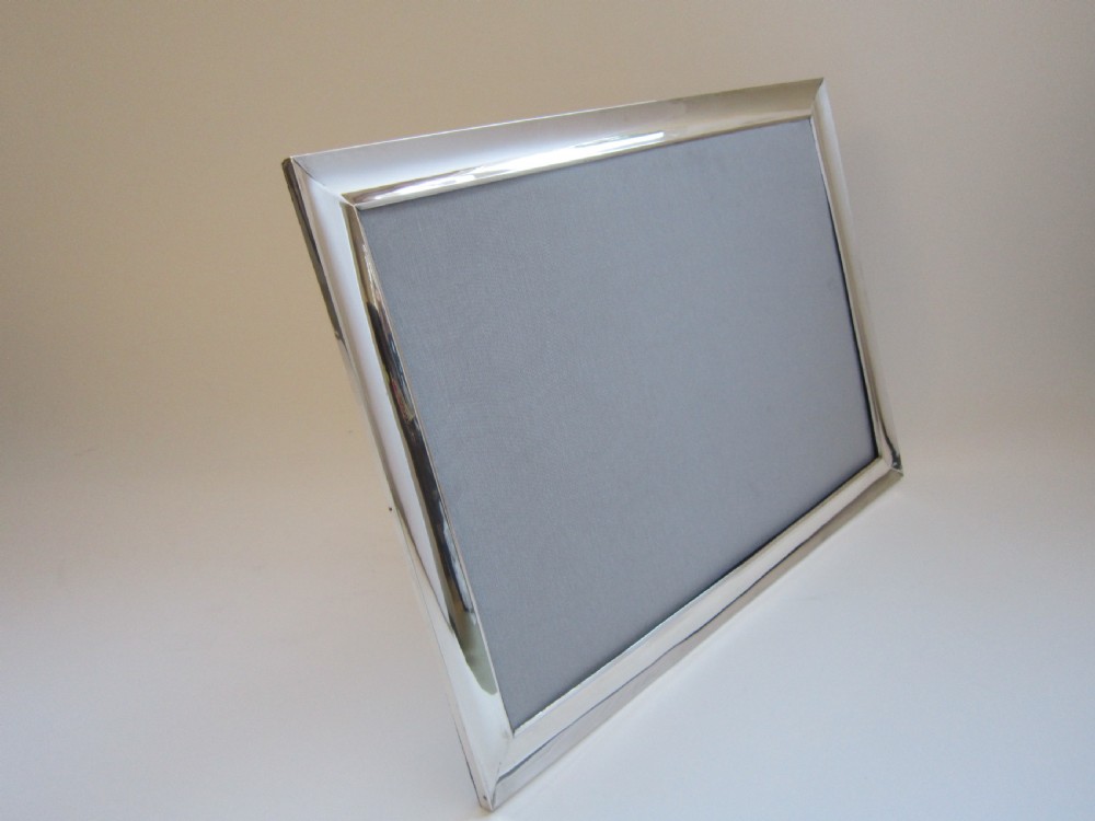 A large rectangular sterling silver picture frame with a simple moulded border and a grey fabric insert in a landscape alignment. View VIII