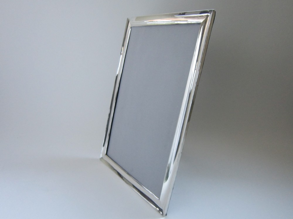 A large rectangular sterling silver picture frame with a simple moulded border and a grey fabric insert in a landscape alignment. View X
