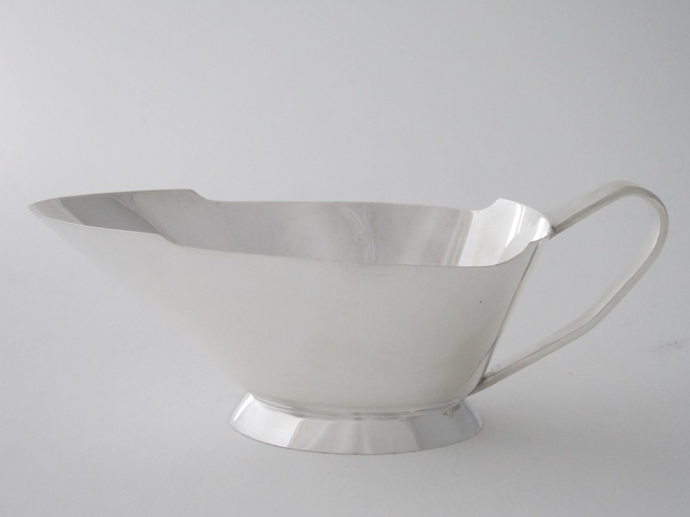 A polished sterling silver Art Deco sauce boat with clean geometric lines, an integrated pouring spout, a loop handle, and a raised oval foot.