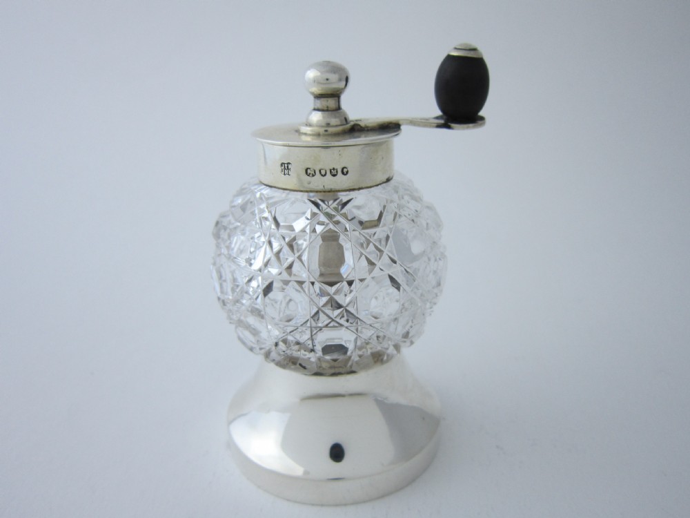 A Victorian sterling silver and cut glass pepper mill with a hand crank handle and hallmarked silver base.