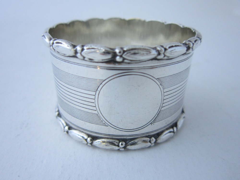A George V sterling silver napkin ring featuring engine-turned line engraving, beaded borders, and a blank circular central cartouche.