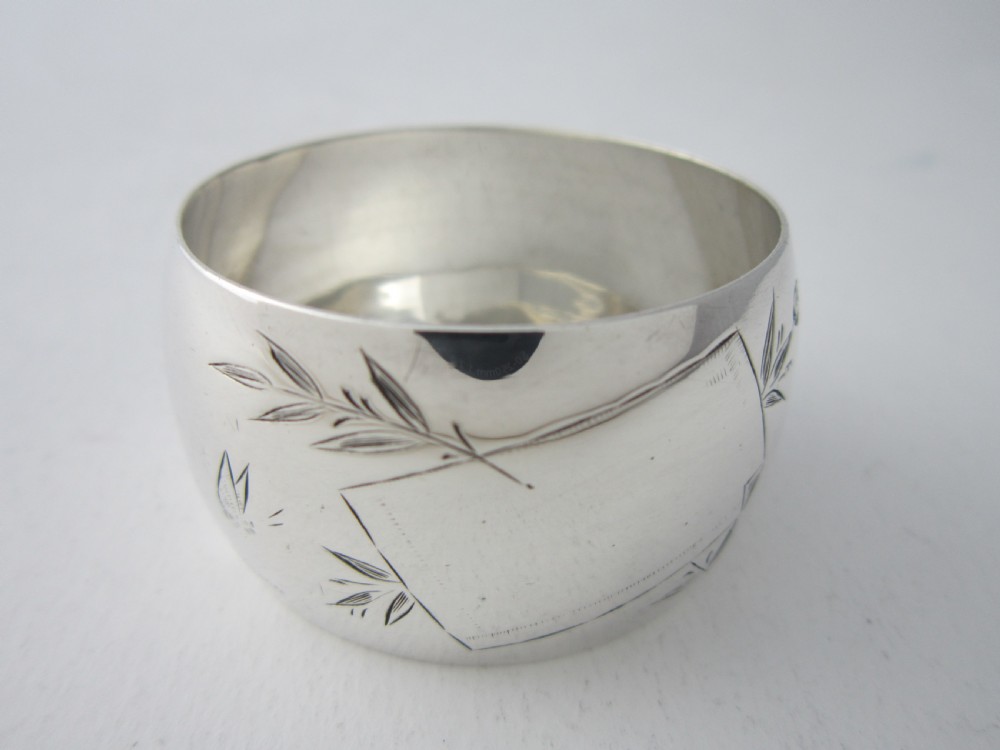 An antique late Victorian sterling silver napkin ring featuring hand-engraved foliate motifs and a polished finish.