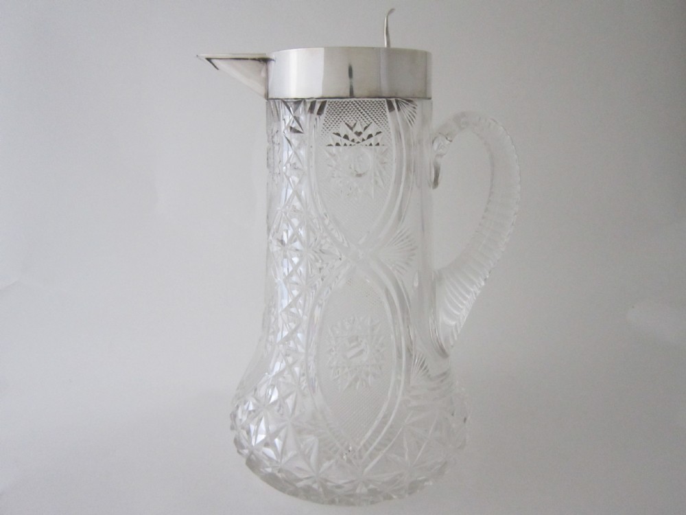 An Edwardian silver-mounted clear cut glass jug featuring geometric diamond carving, a notched glass handle, and a polished sterling silver spout.