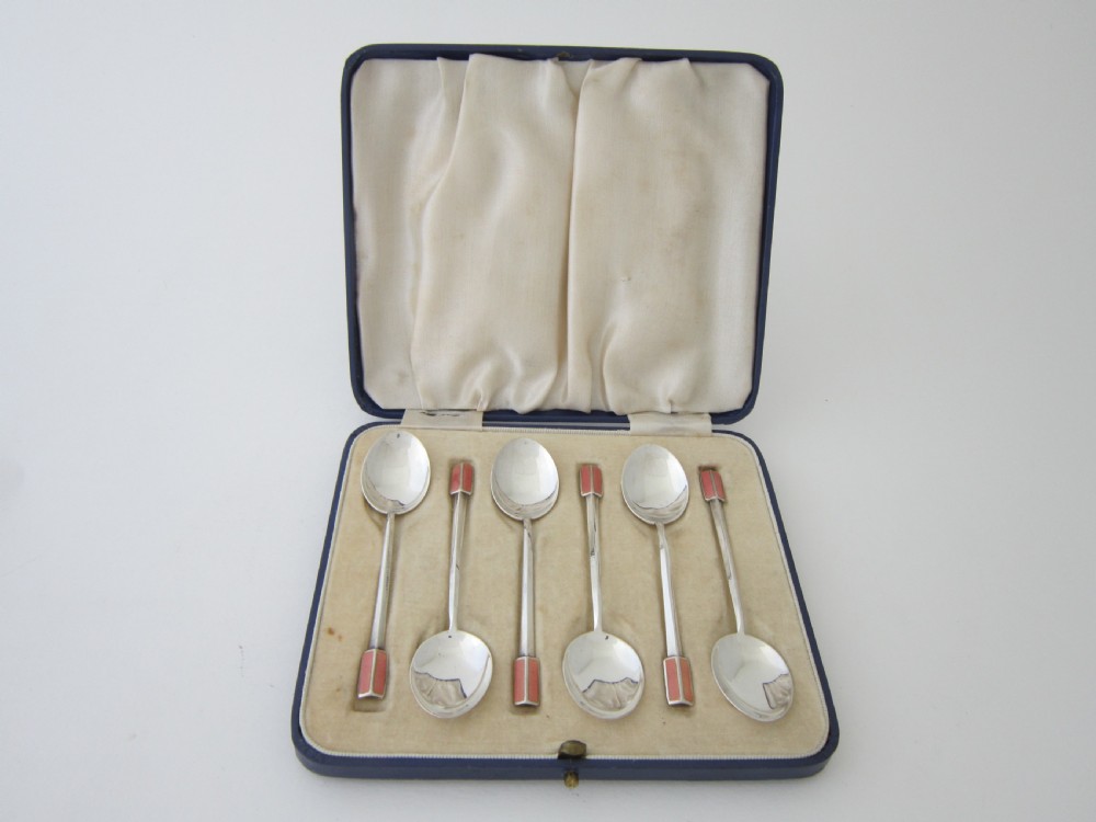 A set of six Art Deco sterling silver coffee spoons with pink enamel terminals presented in an open blue silk-lined case.