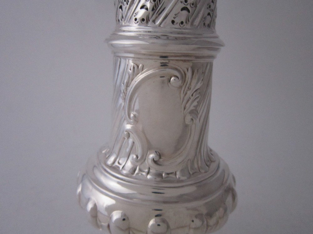 A Victorian sterling silver sugar caster with a spiralled finial, a hand-pierced cap, and a decorated baluster-shaped body. View VI