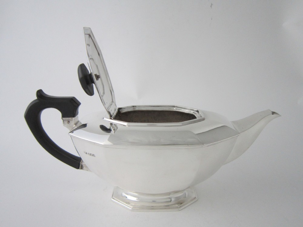 An octagonal sterling silver teapot featuring a carved black wooden handle and matching black lid finial, resting on a faceted pedestal base. View IV