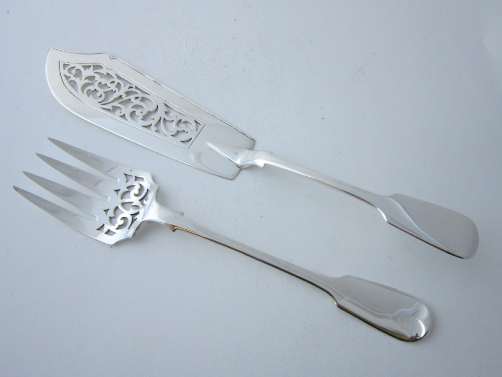 A pair of Victorian sterling silver fish servers featuring a pierced scrollwork knife blade and a four-tine fork with fiddle pattern handles.