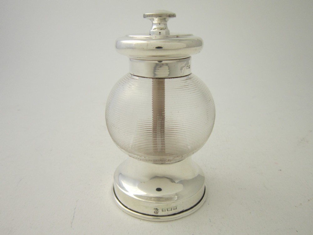 An Edwardian sterling silver and ribbed clear glass pepper grinder with hallmarked silver mounts on the top and base.