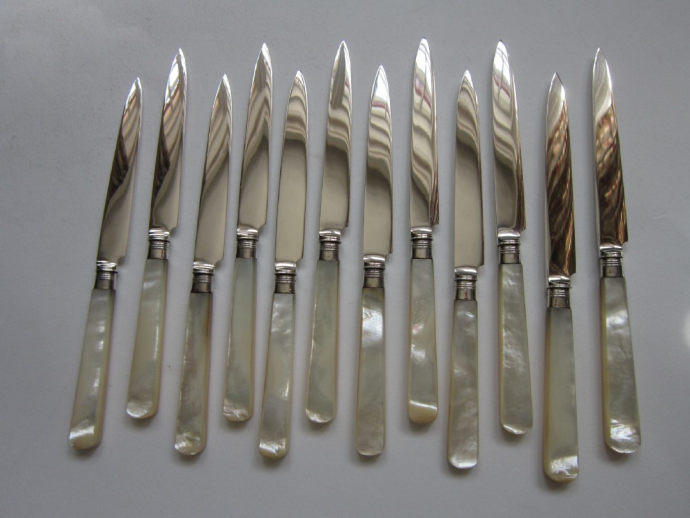 An open fitted wooden canteen lined with green velvet, containing a set of sterling silver dessert knives and forks with carved mother-of-pearl handles. View II