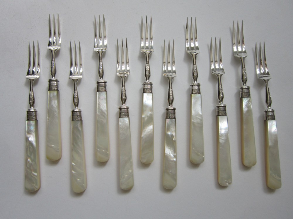 An open fitted wooden canteen lined with green velvet, containing a set of sterling silver dessert knives and forks with carved mother-of-pearl handles. View IV