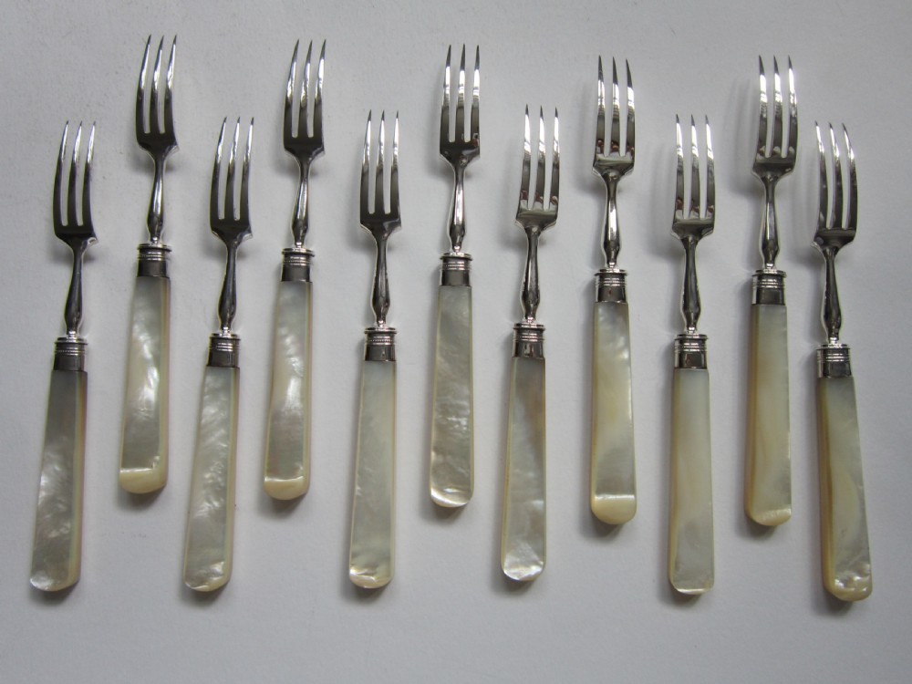 An open fitted wooden canteen lined with green velvet, containing a set of sterling silver dessert knives and forks with carved mother-of-pearl handles. View V