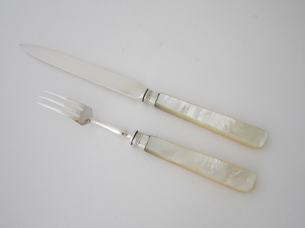An open fitted wooden canteen lined with green velvet, containing a set of sterling silver dessert knives and forks with carved mother-of-pearl handles. View VII