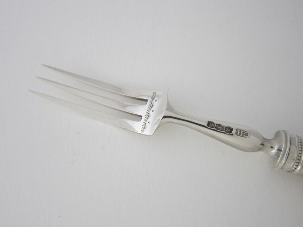 An open fitted wooden canteen lined with green velvet, containing a set of sterling silver dessert knives and forks with carved mother-of-pearl handles. View X