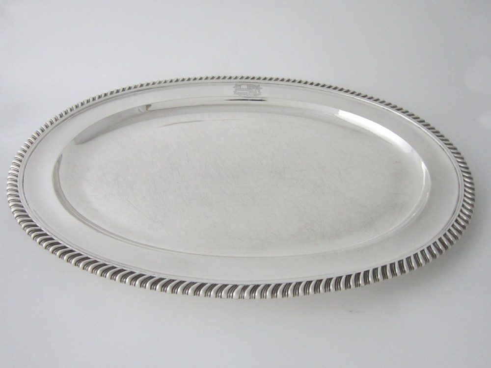 An oval William IV sterling silver meat platter featuring a gadrooned rim and an engraved heraldic coat of arms.