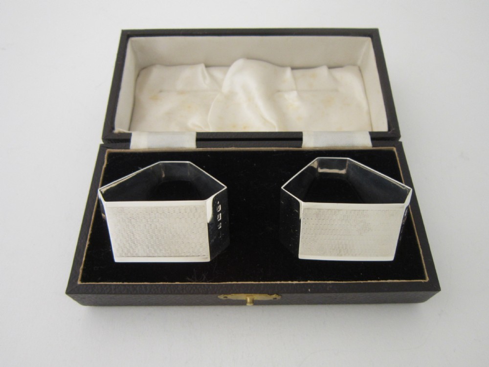 A pair of faceted sterling silver Art Deco napkin rings with subtle engine-turned patterning, presented in a fitted black display box with a cream satin lining.
