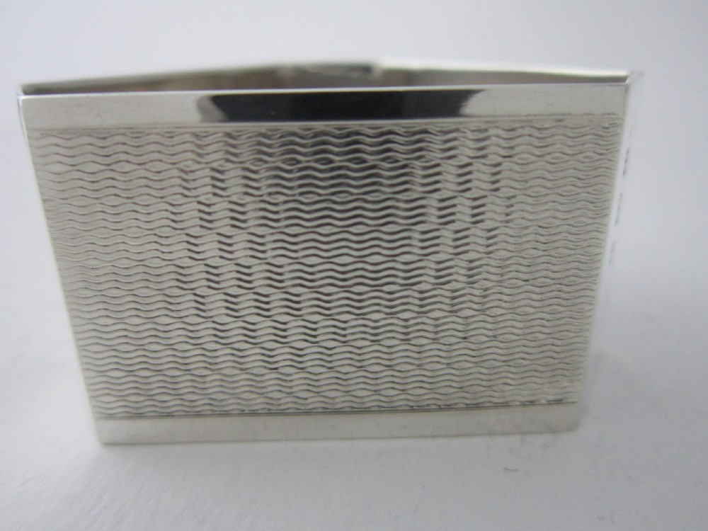 A pair of faceted sterling silver Art Deco napkin rings with subtle engine-turned patterning, presented in a fitted black display box with a cream satin lining. View VII