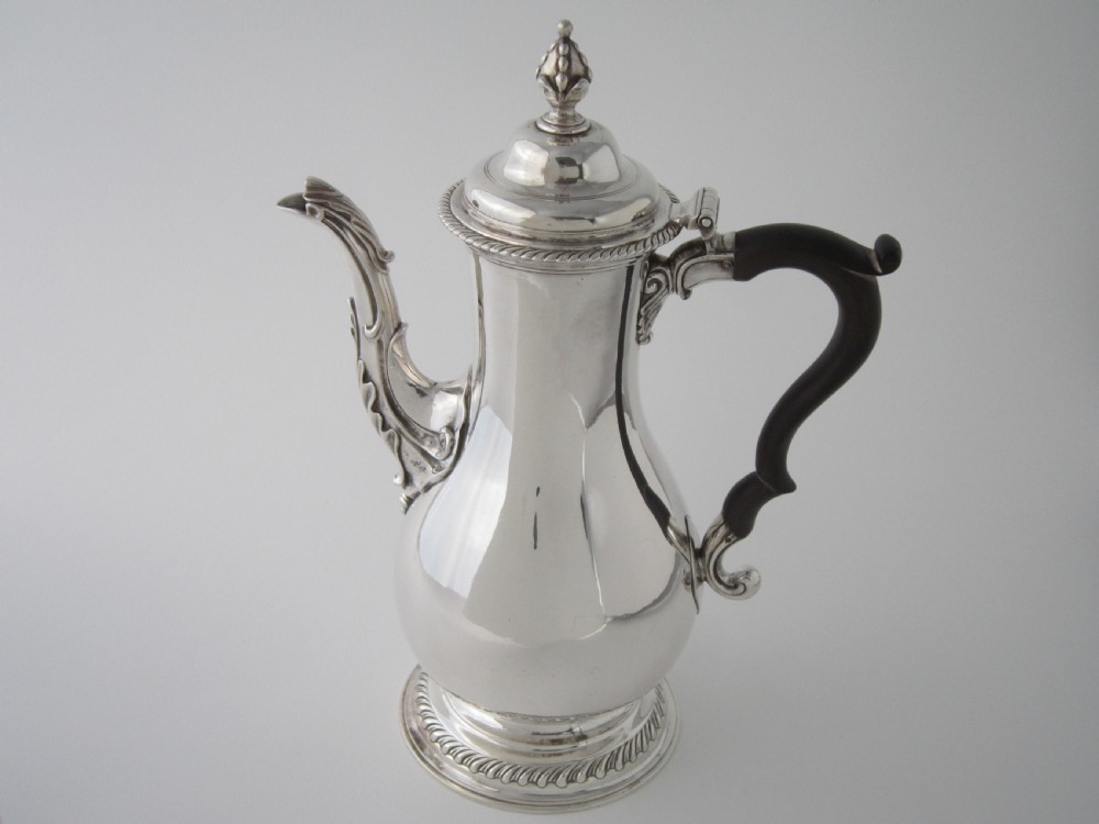 A George III sterling silver coffee pot with a baluster body, carved wooden handle, gadrooned base border, and an ornate cast spout. View II