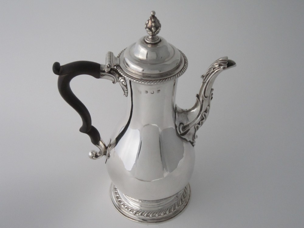A George III sterling silver coffee pot with a baluster body, carved wooden handle, gadrooned base border, and an ornate cast spout. View III