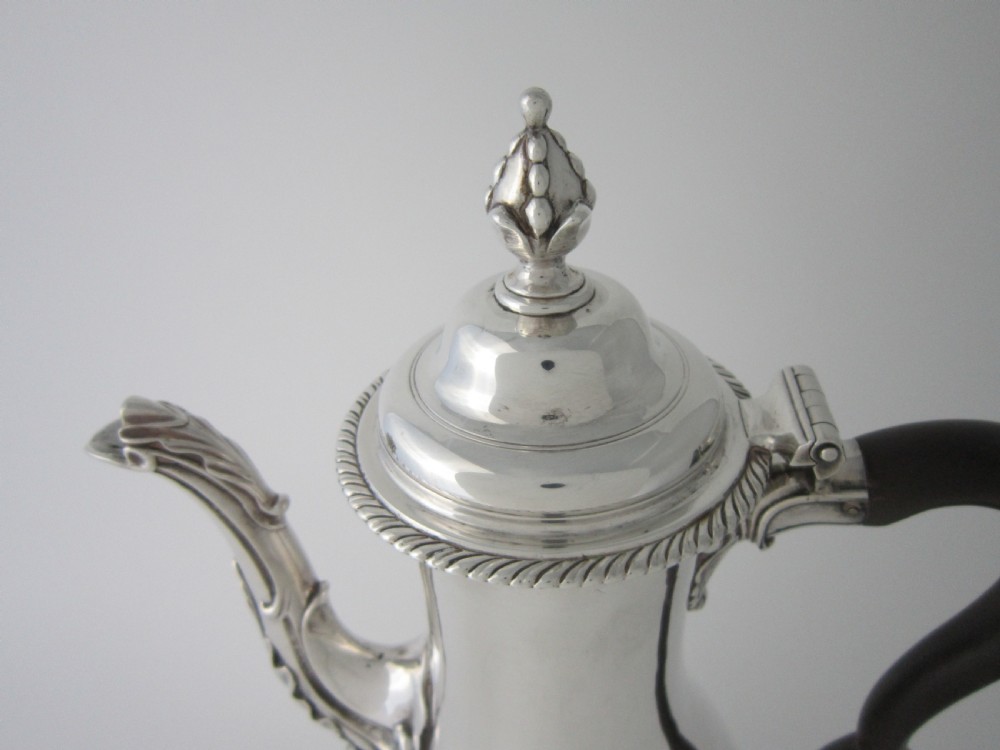 A George III sterling silver coffee pot with a baluster body, carved wooden handle, gadrooned base border, and an ornate cast spout. View IV