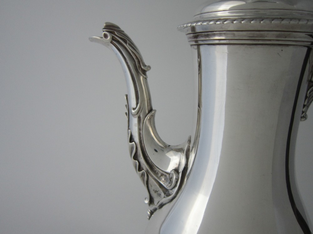 A George III sterling silver coffee pot with a baluster body, carved wooden handle, gadrooned base border, and an ornate cast spout. View V