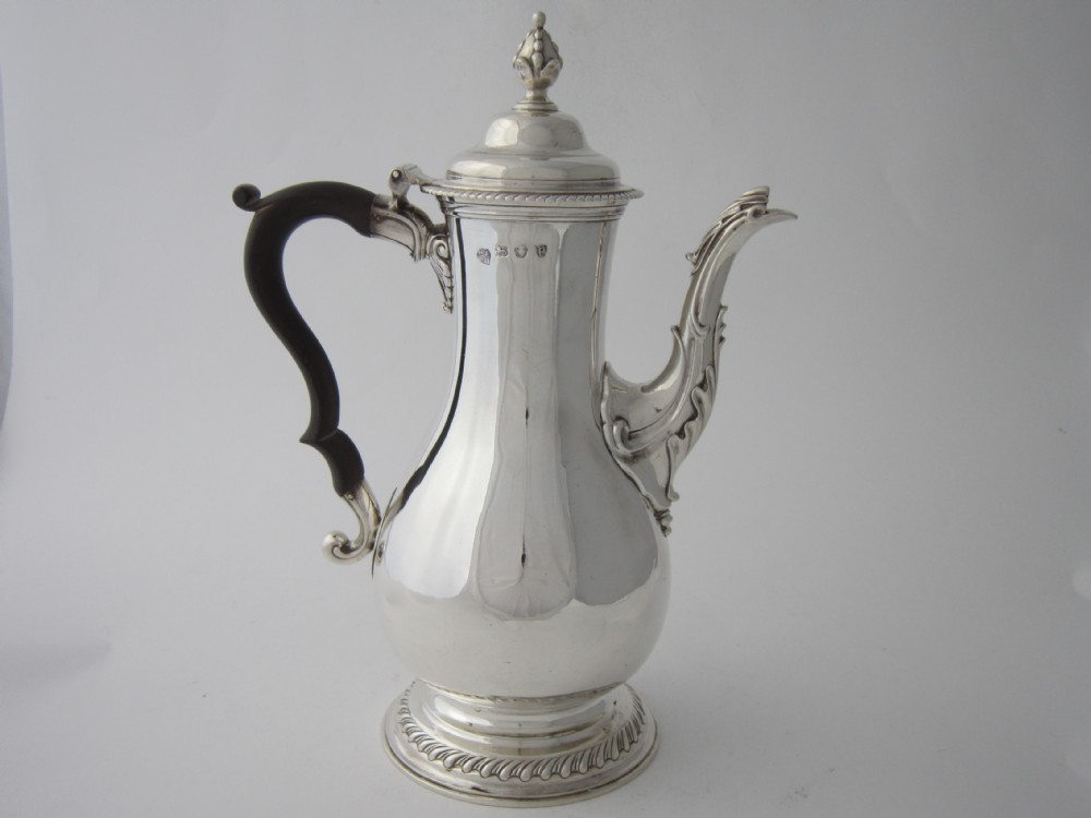A George III sterling silver coffee pot with a baluster body, carved wooden handle, gadrooned base border, and an ornate cast spout.