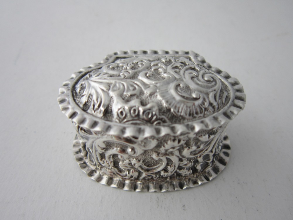 A small Victorian sterling silver pill box decorated with embossed scrollwork and a crimped frilled rim.