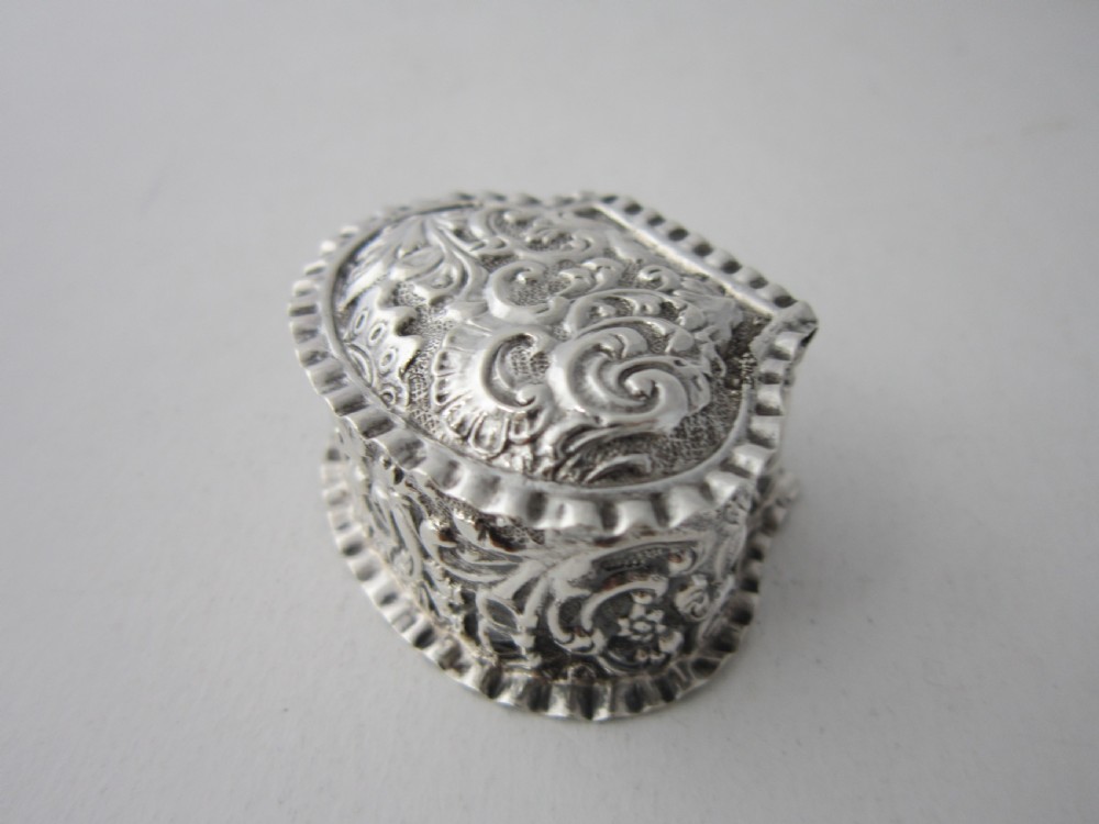 A small Victorian sterling silver pill box decorated with embossed scrollwork and a crimped frilled rim. View II