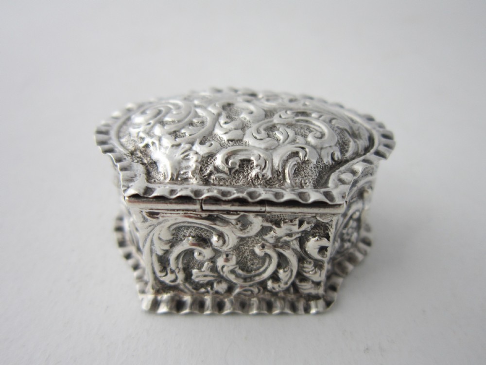 A small Victorian sterling silver pill box decorated with embossed scrollwork and a crimped frilled rim. View III
