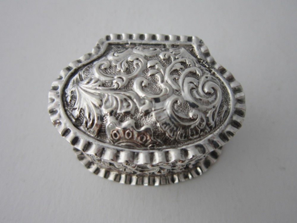 A small Victorian sterling silver pill box decorated with embossed scrollwork and a crimped frilled rim. View IV