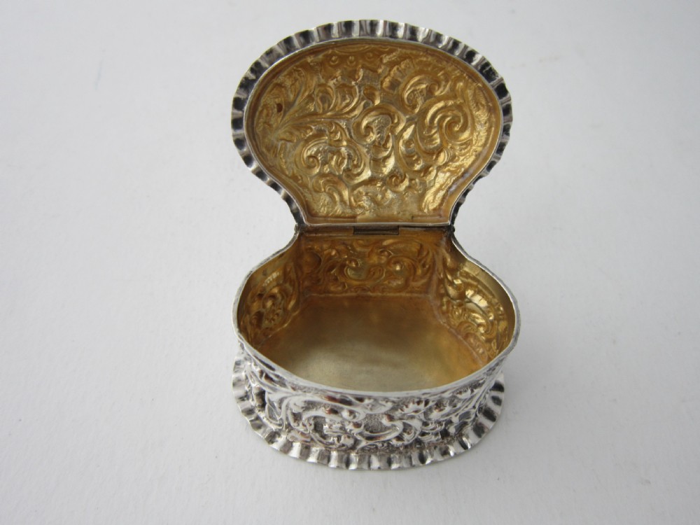 A small Victorian sterling silver pill box decorated with embossed scrollwork and a crimped frilled rim. View V