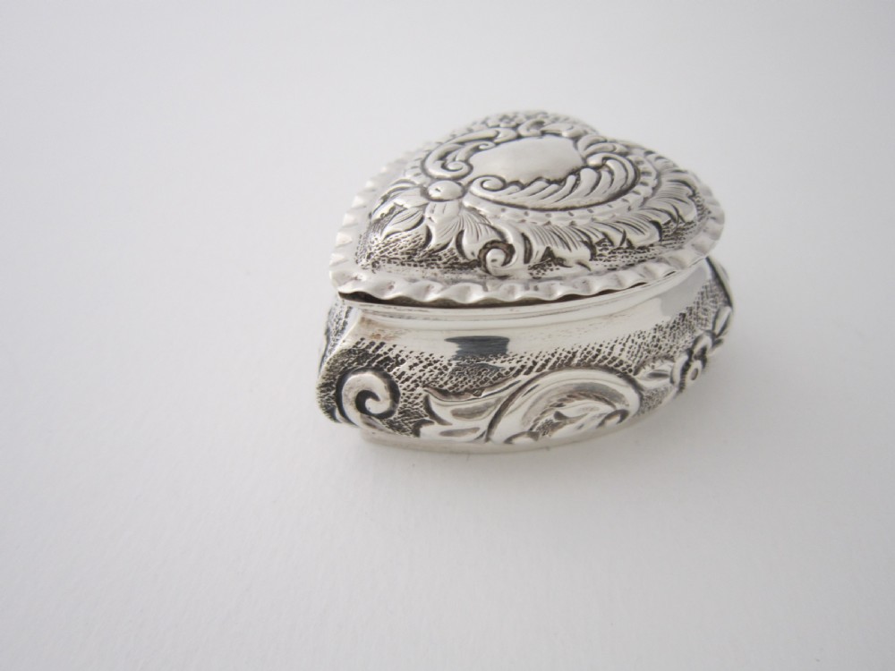 A heart-shaped sterling silver trinket box with detailed embossed foliate scrollwork and a scalloped rim. View II