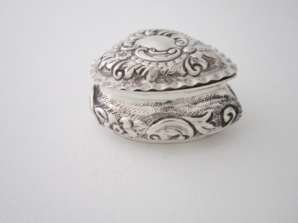 A heart-shaped sterling silver trinket box with detailed embossed foliate scrollwork and a scalloped rim. View III