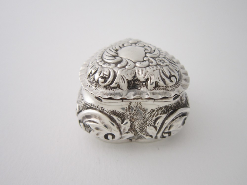 A heart-shaped sterling silver trinket box with detailed embossed foliate scrollwork and a scalloped rim. View IV