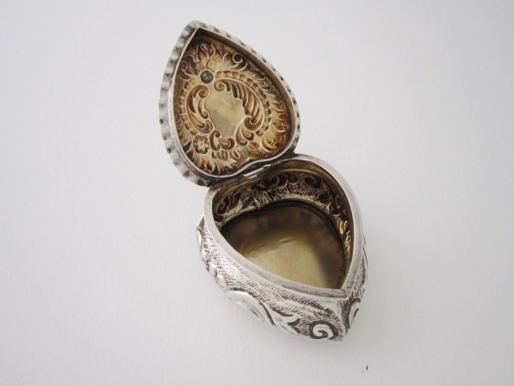 A heart-shaped sterling silver trinket box with detailed embossed foliate scrollwork and a scalloped rim. View V