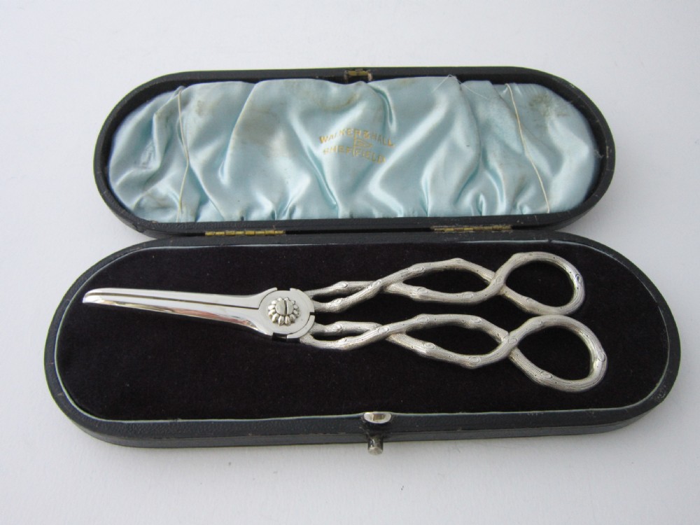 A pair of Victorian sterling silver grape scissors with grapevine-textured handles, resting inside an open fitted presentation case.